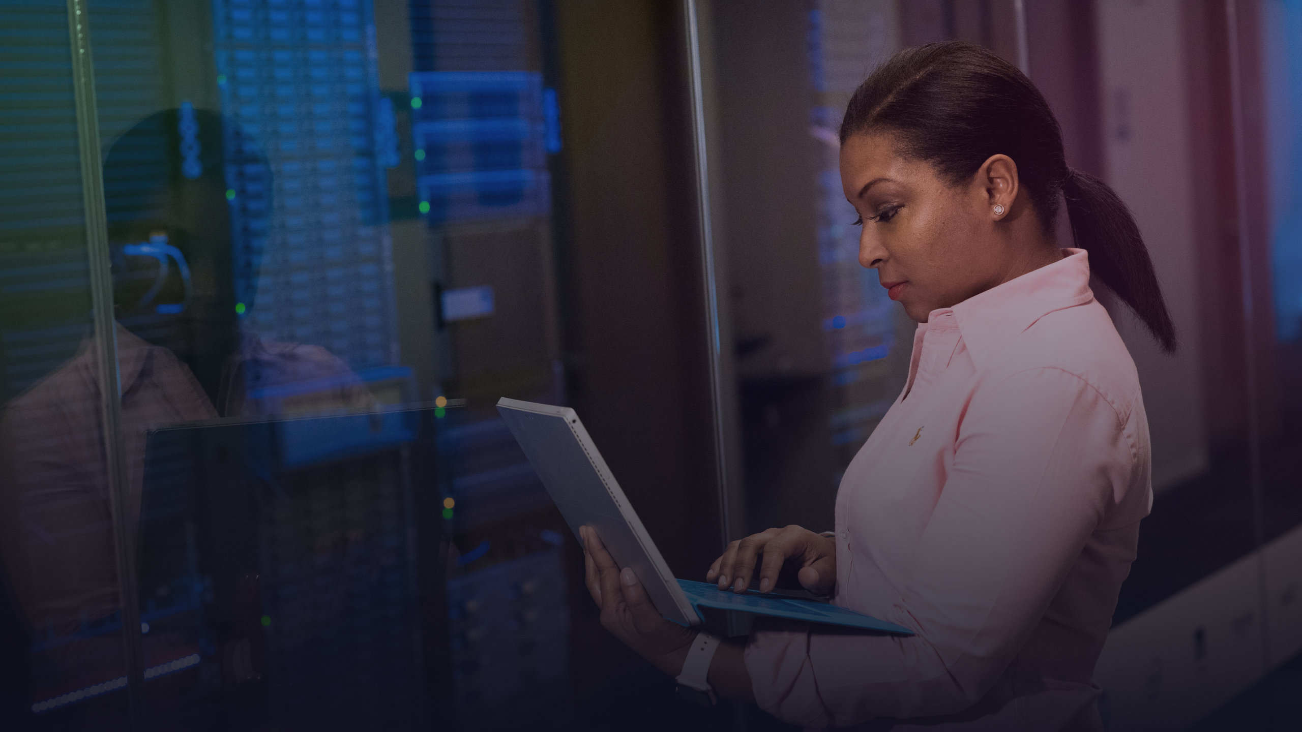 A woman works on a laptop in front of server racks.