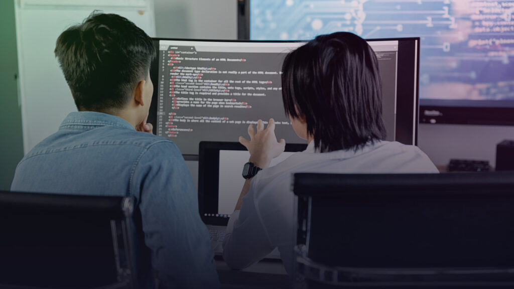 Zwei Entwickler betrachten Programmcode auf mehreren Bildschirmen.