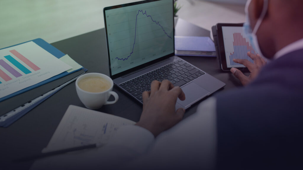 Person nutzt Laptop und Tablet neben gedruckten Diagrammen.