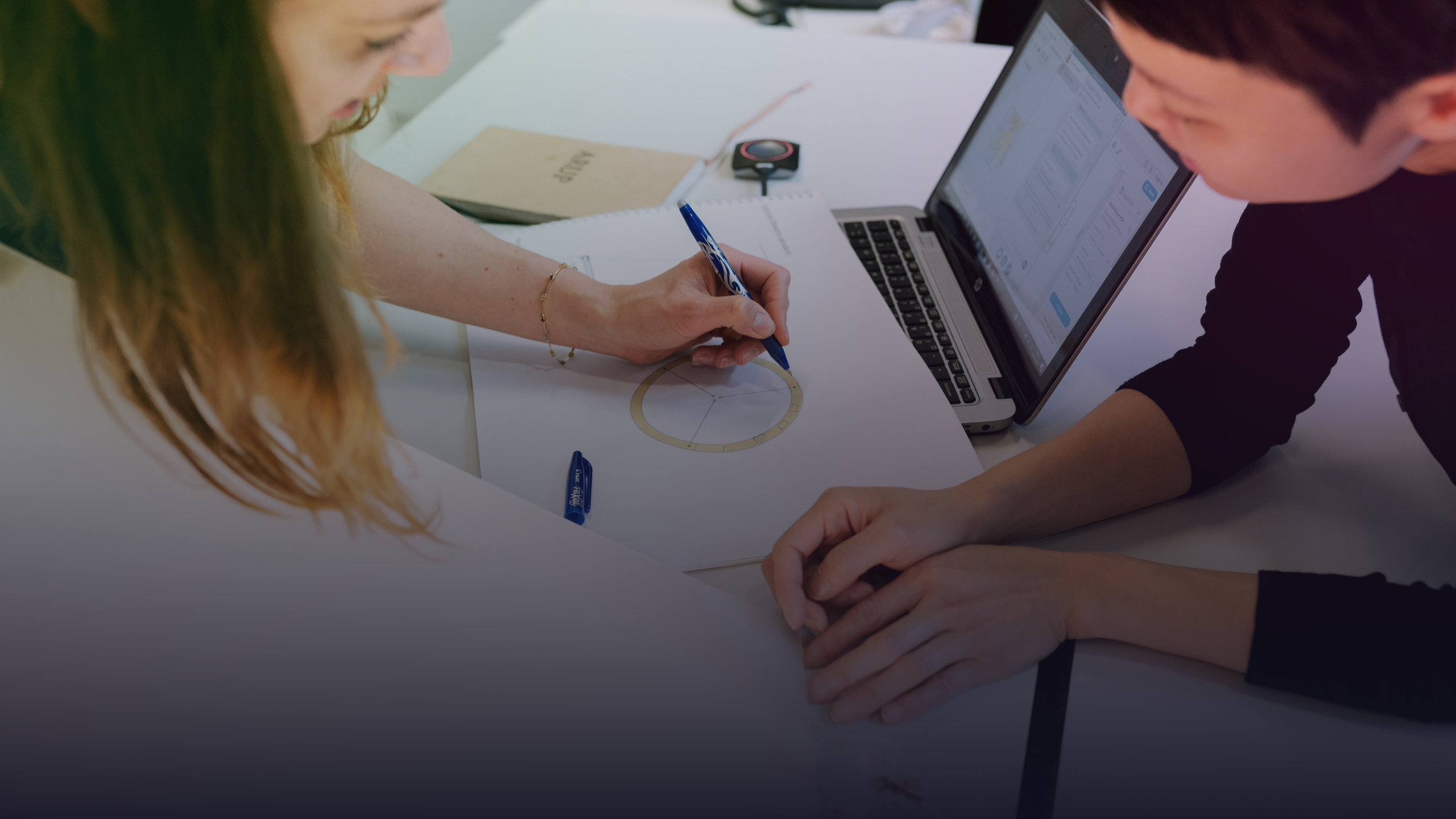 Zwei Ingenieurinnen besprechen Entwürfe und einen Laptop.