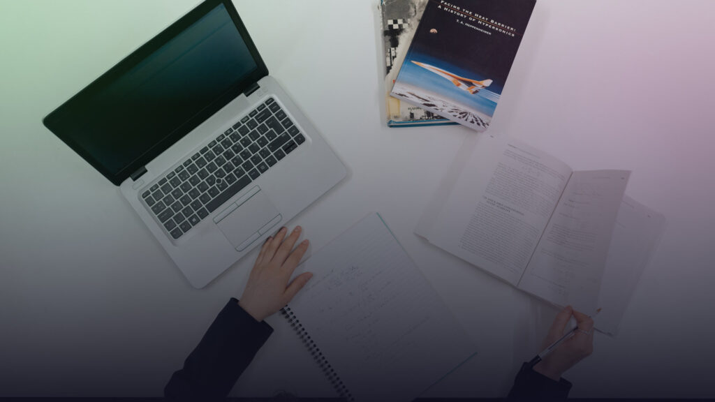Arbeitsplatz mit Laptop, Büchern und handschriftlichen Notizen.