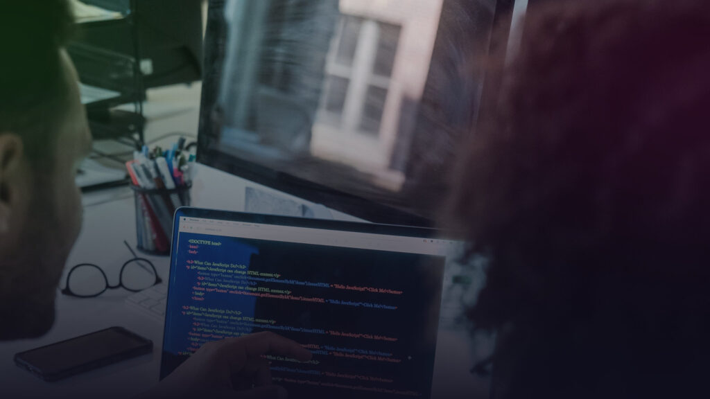 Zwei Personen prüfen gemeinsam Programmcode auf einem Bildschirm.