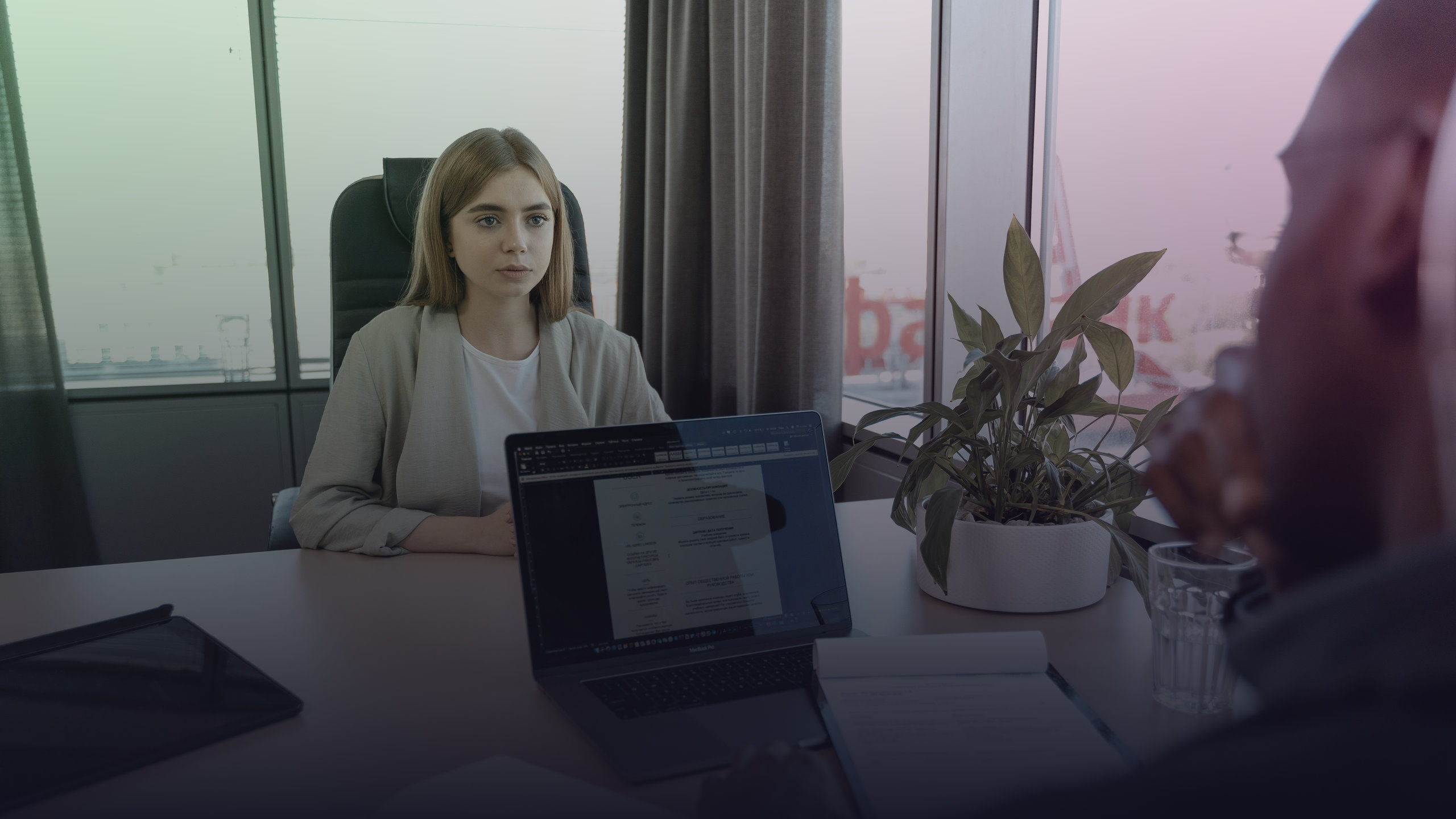 A candidate talks with an interviewer at a desk with a laptop.
