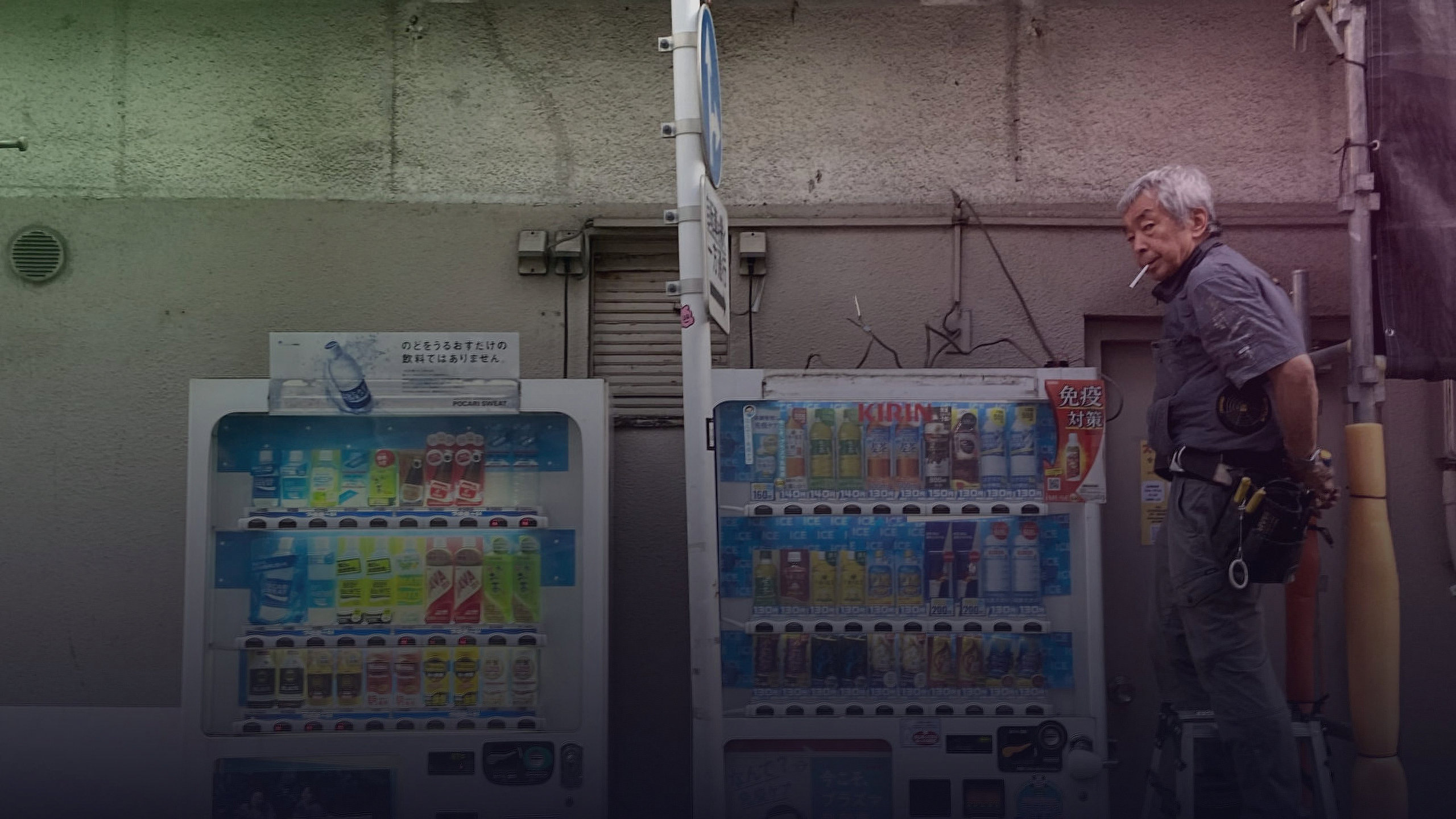 Ein Mann steht neben zwei Getränkeautomaten an einer Hauswand.
