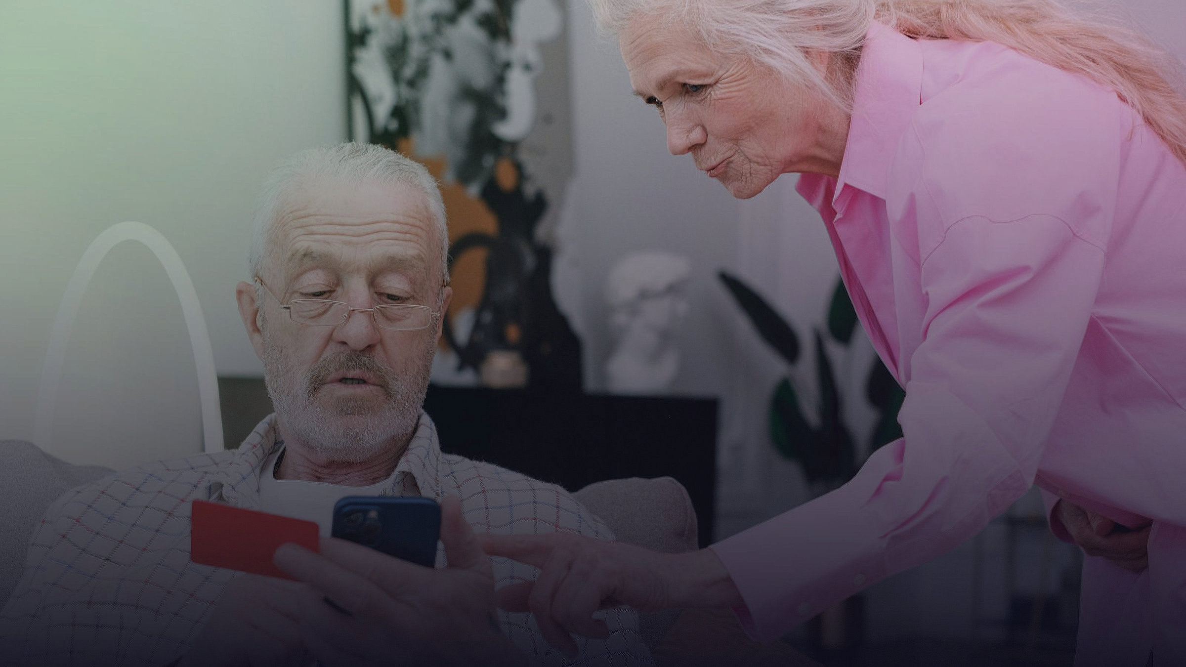 A care worker helps an elderly man with a digital payment on a smartphone.