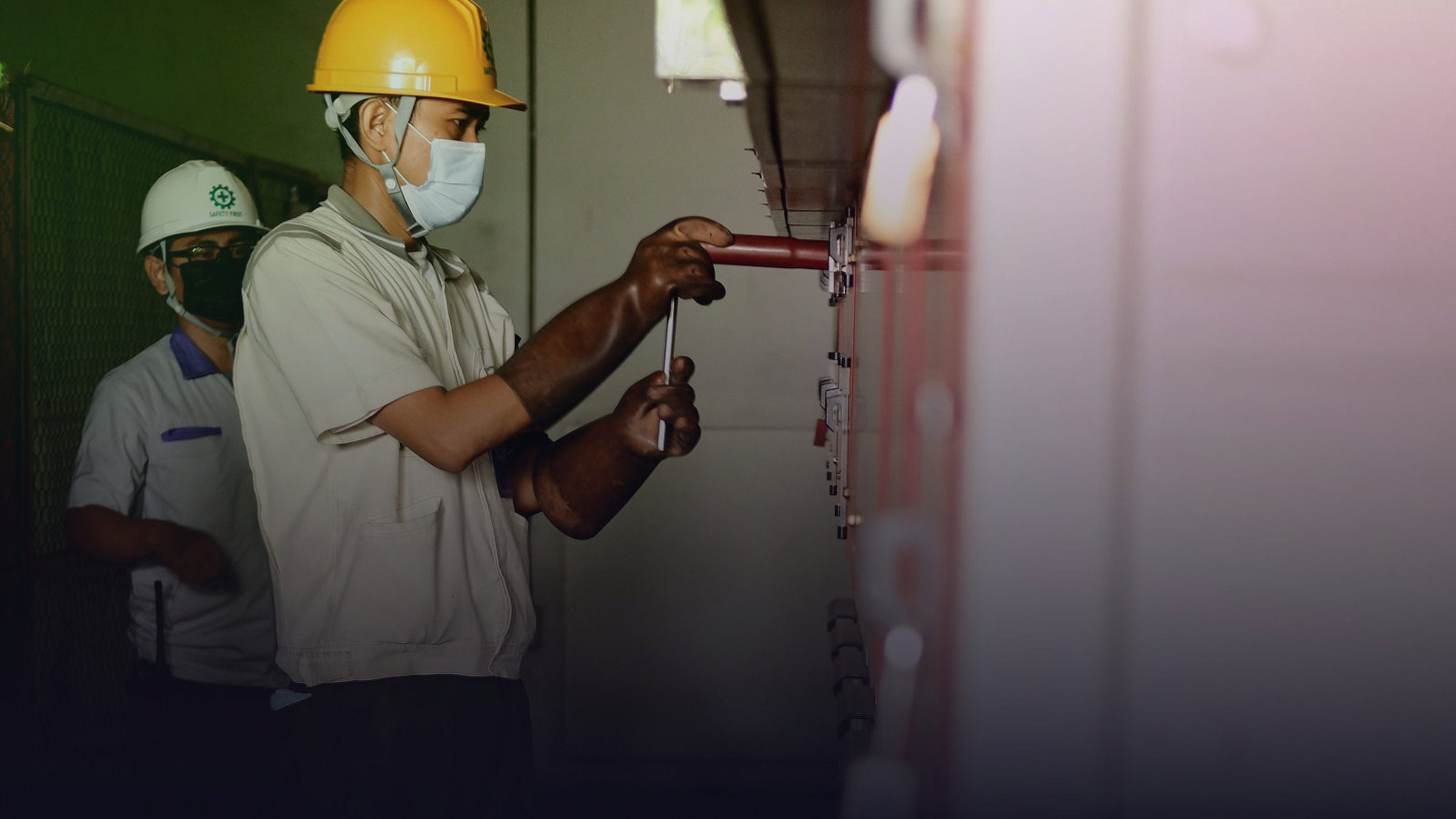 Two technicians in protective gear work on industrial equipment.