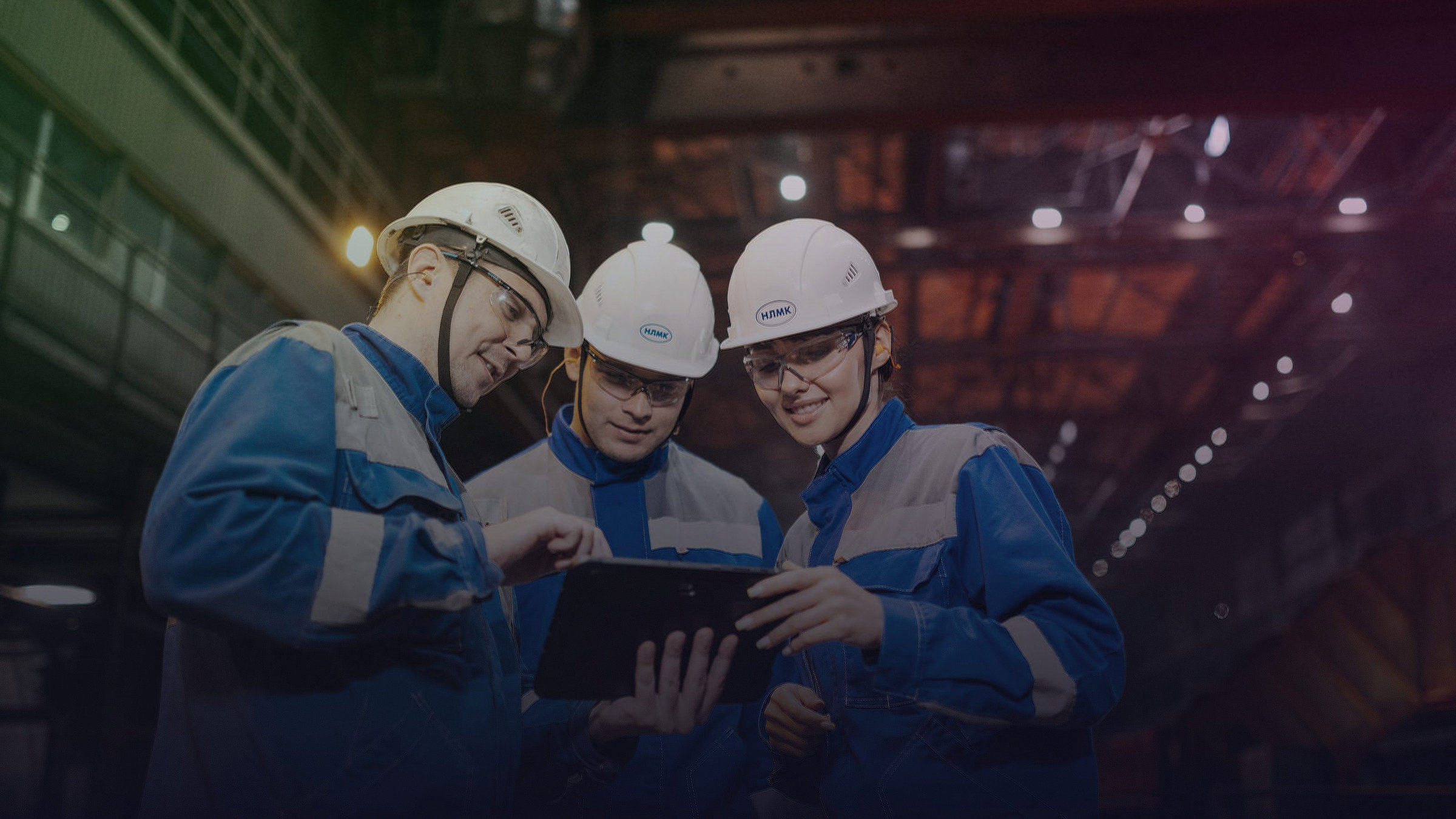 Drei Mitarbeitende in Schutzausrüstung besprechen Daten auf einem Tablet in einer Industrieanlage.