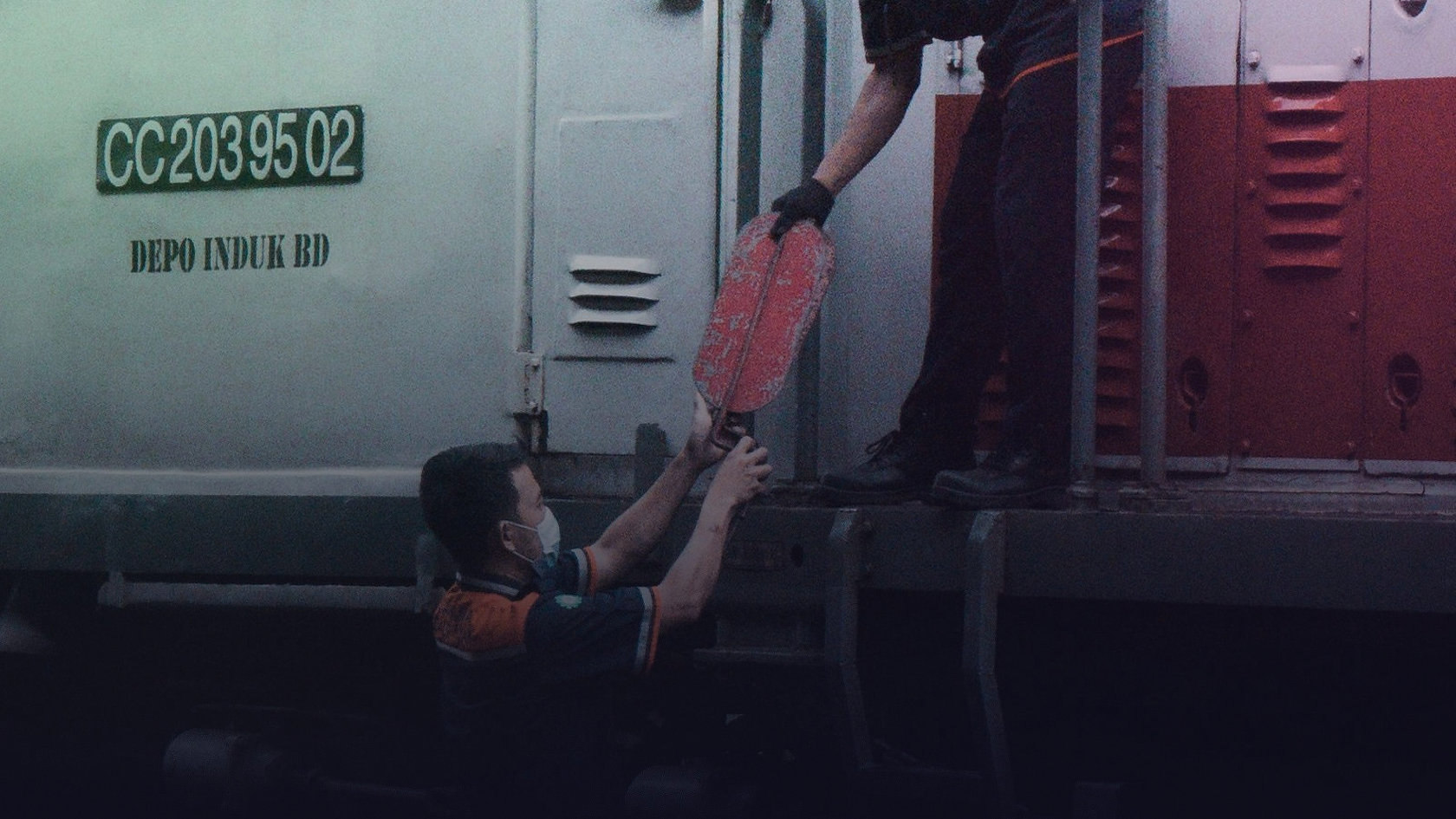 Two technicians pass a tool to each other on a rail vehicle.