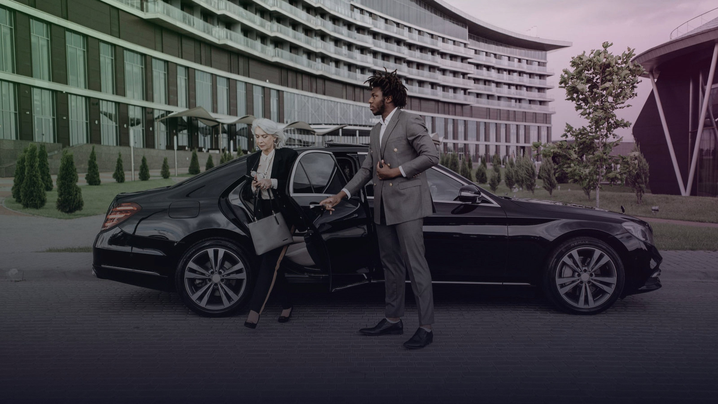 A man holds a car door open as a woman steps out of a black saloon.