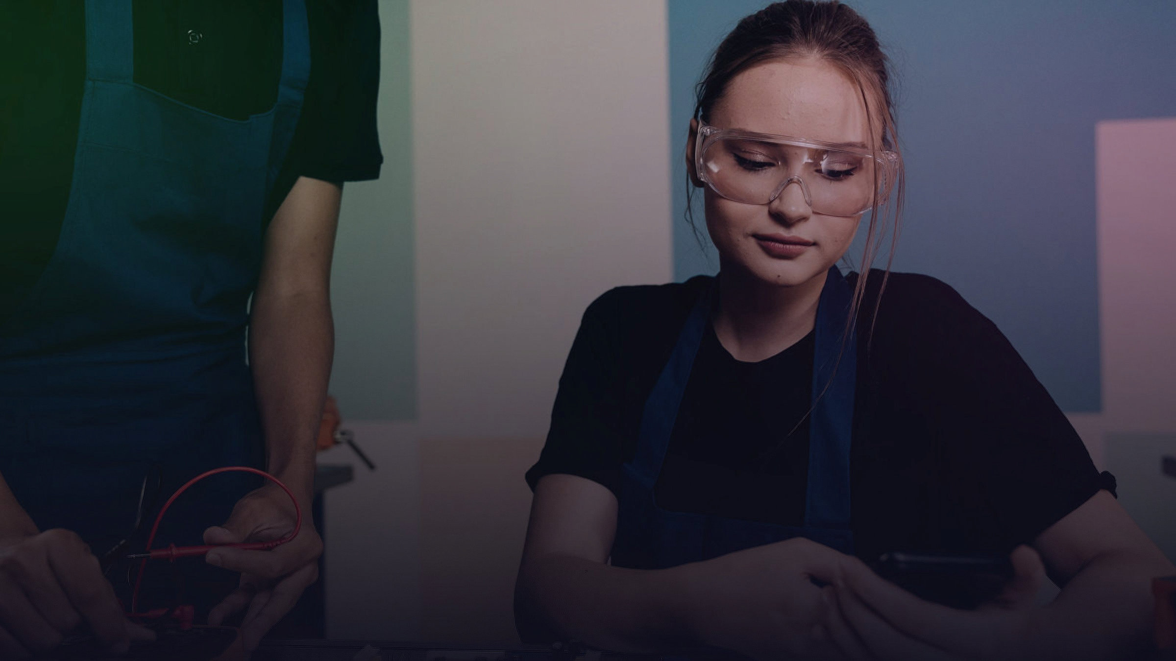 Zwei Personen mit Schutzbrille prüfen ein elektronisches Bauteil.